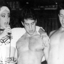 An announcer and two shirtless men on stage.